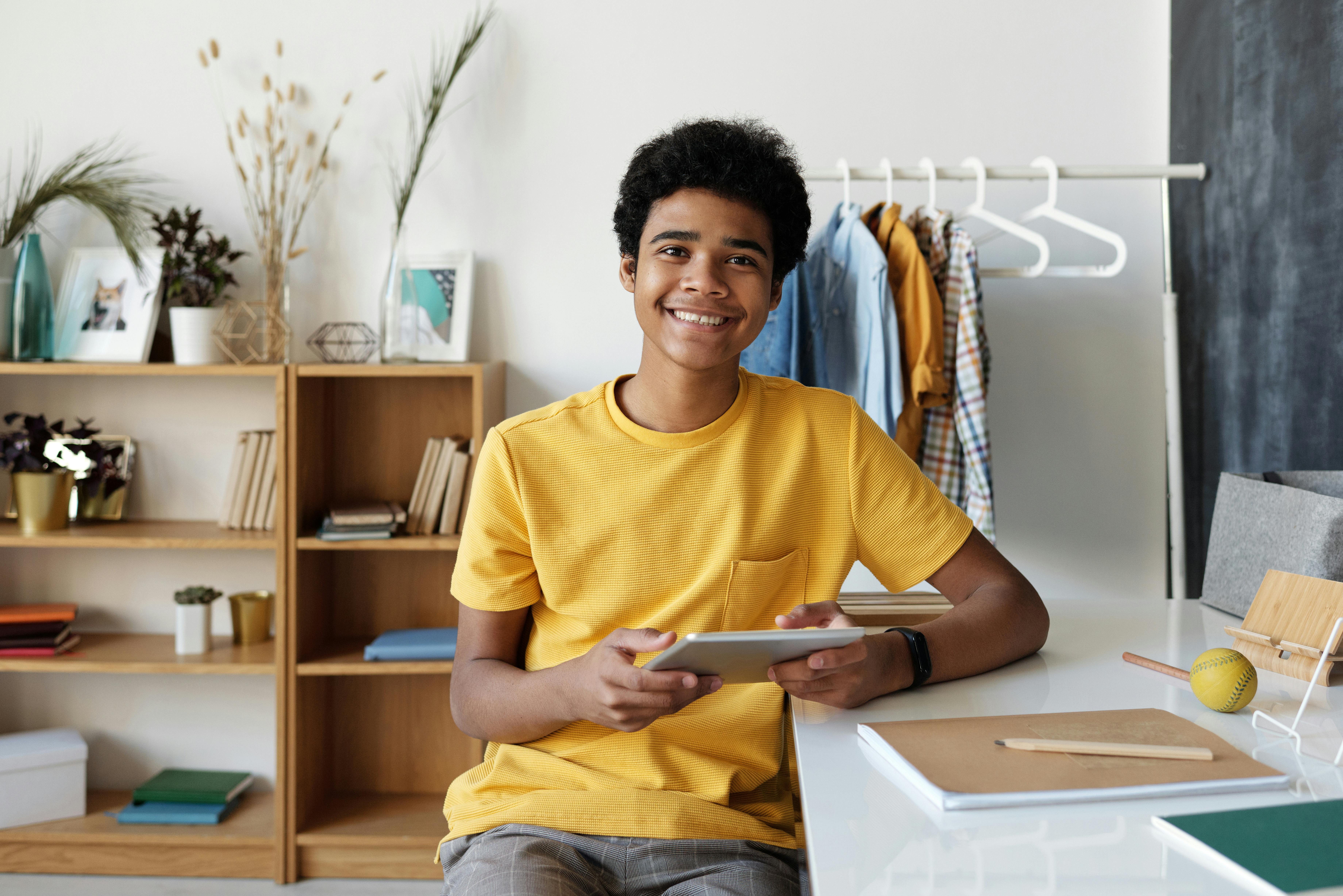 Smiling teenager using a tablet at his desk for online learning at home.