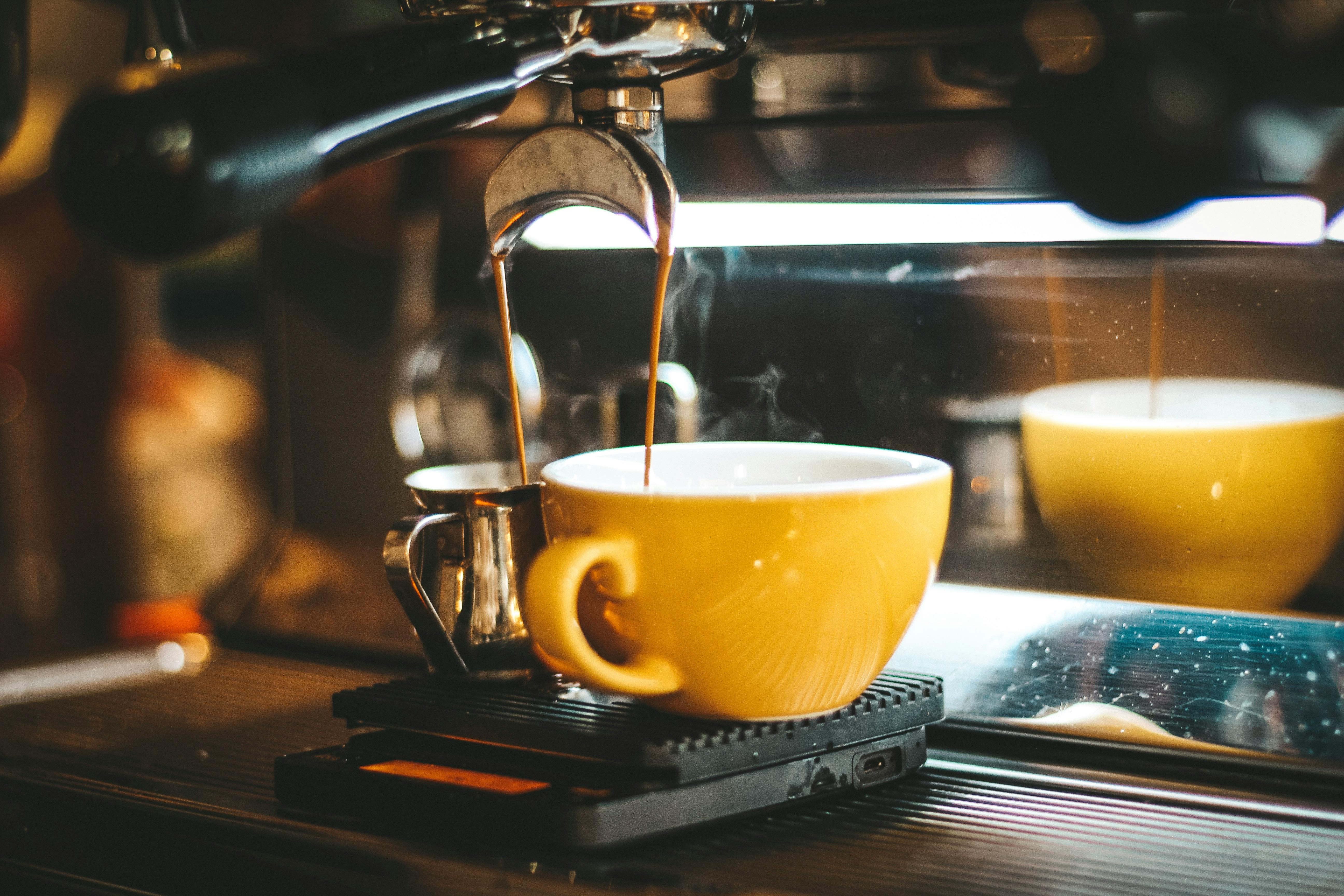 Steaming espresso pours into a yellow cup in a cozy café.
